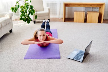 Dizüstü bilgisayarda, kopya alanı Eğitim Online egzersiz için sırt üstü yere vasıl ev, yapmak güzel ve genç birbayan. Tam uzunlukta portre. Çalışma dışarı egzersiz yoga, pilates,