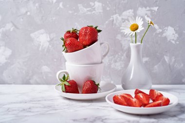 Olgun organik çilek kopya alanı gri beton zemin üzerine vazoda beyaz seramik kase ve papatya çiçekler içinde. Sağlıklı gıda kavramı, natürmort