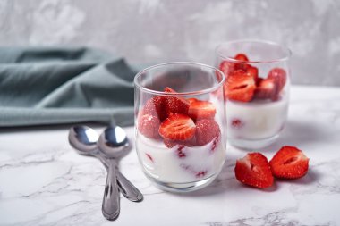 İki bardak taze dilimlenmiş çilek, kaşık ve beyaz mermer zemin, peçeteye tablo ile sağlıklı yoğurt uzay kopyalayın. Sağlıklı Kahvaltı, gıda kavramı