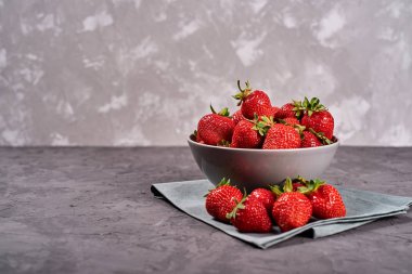 Kırmızı çilek seramik kasede keten masa peçetesinin üzerinde gri beton arka planda, kopyalama alanı. Sağlıklı gıda konsepti, natürmort