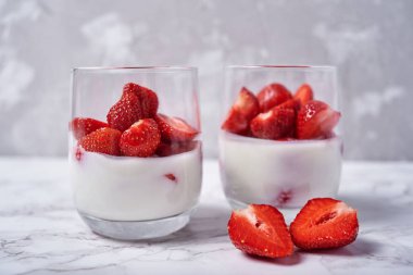 Sağlıklı taze dilimlenmiş çilek beyaz üzerine yoğurtlu iki kadeh tabloda arka plan, kopya alanı mermer. Sağlıklı Kahvaltı, gıda kavramı