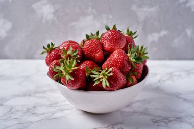 Organik olgun çilek kopya alanı gri mermer zemin üzerine beyaz seramik kase. Sağlıklı gıda kavramı, natürmort