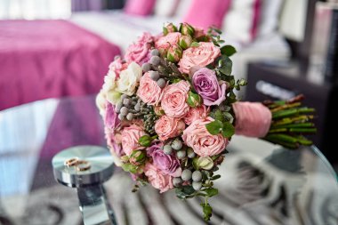 Yemyeşil gelin pembe buket kadar yakın ve saten şerit ve iki altın yüzük Mor gül cam masa arka plan üzerinde kapalı, kopya alanı bulanıklık. Düğün kavramı 