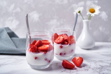 Sağlıklı yoğurtlu taze dilimlenmiş çilek, kaşık, papatya çiçeği vazo ve tablo peçeteye beyaz mermer zemin, kopya alanı üzerine iki kadeh. Sağlıklı Kahvaltı, gıda kavramı