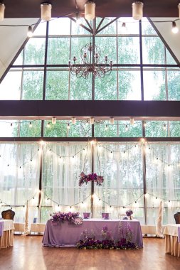 Presidyum restoranda düğün, uzay kopyalayın. Ziyafet masa yeni çiçekler, monstera yaprakları, menekşe kumaş ve ampuller ile evli. Yemyeşil çiçek aranjman. Lüks düğün süslemeleri 