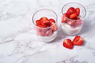 Sağlıklı taze dilimlenmiş çilek beyaz üzerine yoğurtlu iki kadeh tabloda arka plan, kopya alanı mermer. Sağlıklı Kahvaltı, gıda kavramı