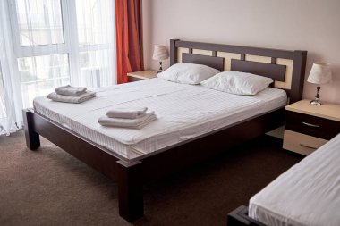 Ahşap yatak başı, komidin ve büyük pencere, kopya alanı boş adet Tek Kişilik Yataklı otel yatak odası iç. Beyaz çarşaf, yumuşak yastık ve yatak havlu