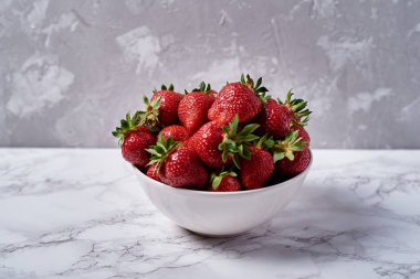 Organik olgun çilek kopya alanı gri mermer zemin üzerine beyaz seramik kase. Sağlıklı gıda kavramı, natürmort