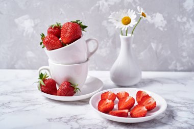 Kırmızı organik çilek Çilek dilimleri ve papatya çiçekler vazoda gri beton zemin üzerine beyaz seramik Kupası uzay kopyalayın. Sağlıklı gıda kavramı, Natürmort