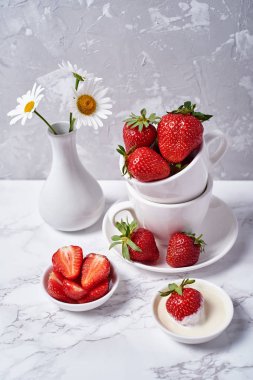 Kırmızı organik çilek beyaz seramik Kupası; Vazoda gri mermer zemin üzerine krema ve papatya çiçekler; kopya alanı. Sağlıklı gıda kavramı; Natürmort