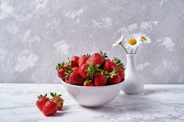Kopya alanı gri beton zemin üzerine vazoda beyaz seramik kase ve papatya çiçekler kırmızı olgun çilek. Sağlıklı gıda kavramı, natürmort