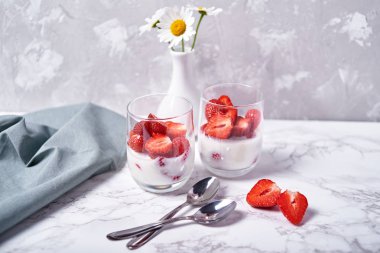 Sağlıklı yoğurtlu taze dilimlenmiş çilek, kaşık, papatya çiçeği vazo ve tablo peçeteye beyaz mermer zemin, kopya alanı üzerine iki kadeh. Sağlıklı Kahvaltı, gıda kavramı