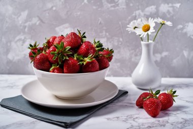 Keten masa peçete ve papatya çiçekler vazoda kopya alanı gri beton zemin üzerine beyaz seramik kase kırmızı organik çilek. Sağlıklı gıda kavramı, Natürmort