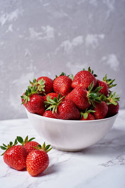 Organic ripe strawberries in white ceramic bowl on gray concrete background, copy space. Healthy food concept, still life