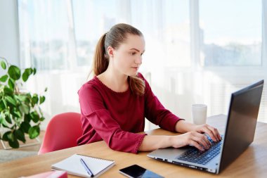 Ahşap masa başında oturan ve modern ofis, kopya alanı dizüstü bilgisayarda yazarak ciddi işkadını portresi