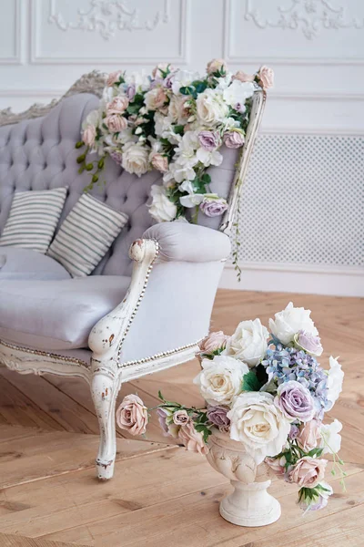 Beautiful bouquet of roses in antiqe vase on floor near sofa with chesterfield upholstery, copy space. Luxury rich living room interior
