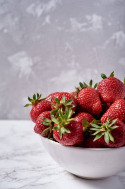 Gri alçı duvar arka plan üzerinde beyaz seramik kase organik olgun çilek, kopya alanı. Sağlıklı gıda kavramı, natürmort