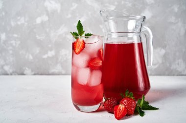 Köpüklü cam buz ve nane ile taze çilek limonata ve beyaz masa arka plan üzerinde sürahi, kopya alanı. Soğuk yaz içkisi. Berry kokteyl