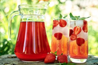 Taze çilek limonata buz ve nane bardak ve yeşil arka plan açık, kopya alanı ile ahşap masada sürahi ile. Soğuk yaz içkisi. Berry kokteyl ile Köpüklü cam