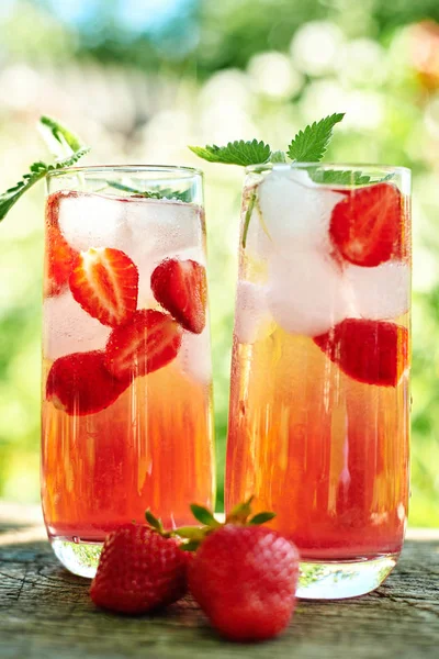新鲜的草莓柠檬水与冰和薄荷在玻璃在木桌上与绿色背景户外 复制空间 冷夏饮料 带浆果鸡尾酒的闪闪发光的玻璃杯 — 图库照片