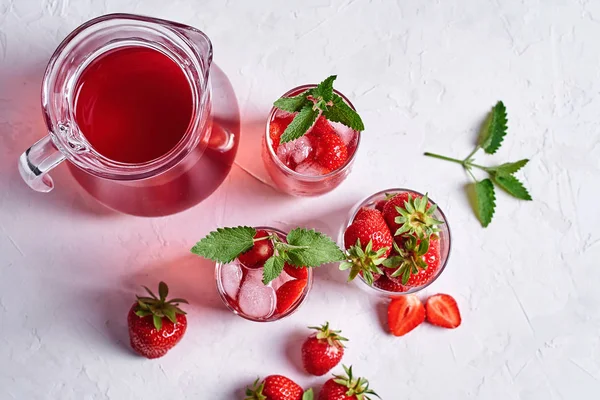 Taze çilek limonata buz ve nane bardak ve beyaz masa arka plan üzerinde sürahi, kopya alanı ile. Soğuk yaz içkisi. Berry kokteylile köpüklü cam. Üst görünüm, düz yatıyordu