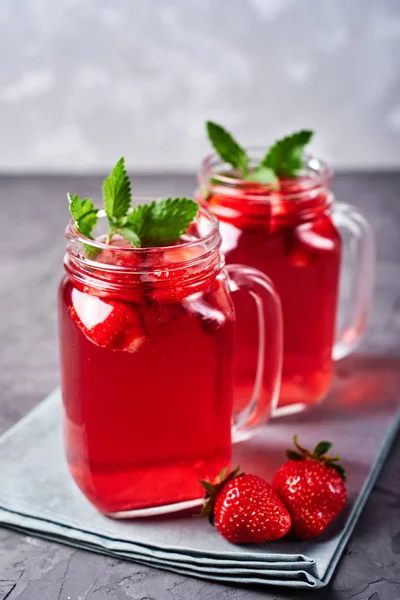 Homemade strawberry lemonade with mint in mason jars on gray concrete table background, copy space. Cold summer berry drink in sparkling glasses. Fresh vitamin beverage