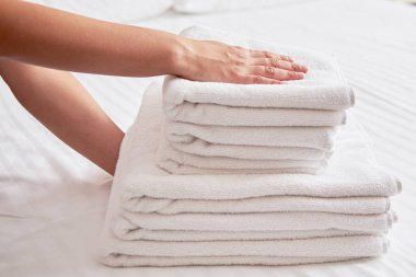 Kadın yatak çarşafı üzerine taze beyaz banyo temiz havlu yığını koyarak, kopya alanı. Otel hizmetçisinin ellerini havluyla kapatın. Oda servisi