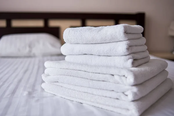 Pilha de toalhas de banho limpas brancas na cama lençol no hotel moderno ser — Fotografia de Stock