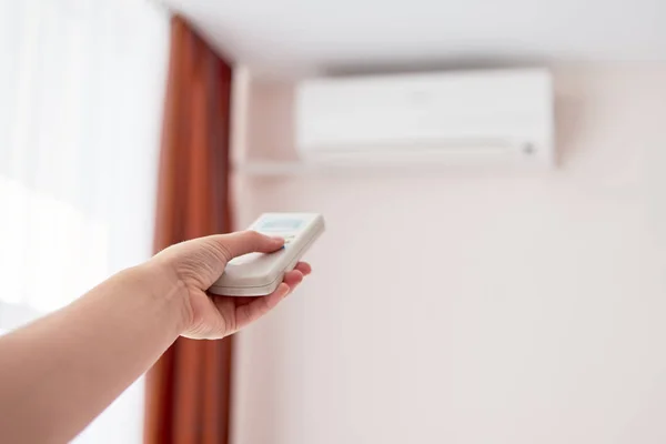 Woman operating remote controller on air conditioner inside the — Stock Photo, Image