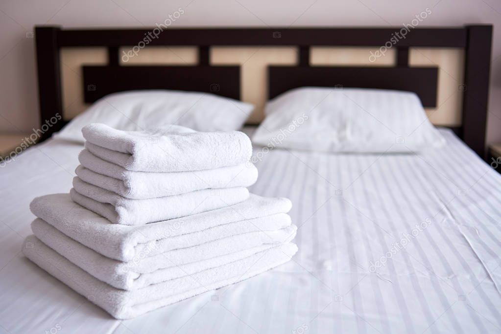 Stack of white clean bath towels on bed sheet in modern hotel be