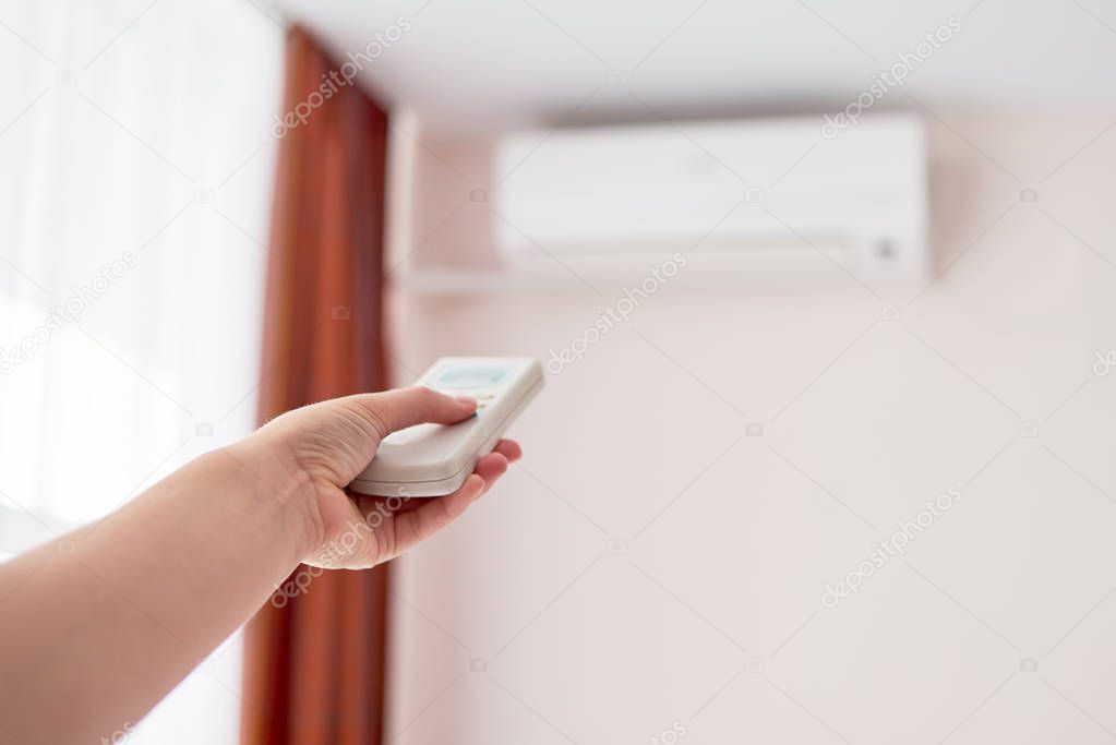 Woman operating remote controller on air conditioner inside the 