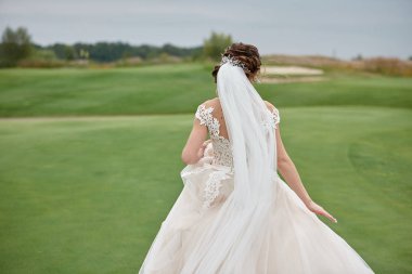 Yeşil golf sahası, arka görünüm üzerinde çalışan modern saç modeli ile beyaz gelinlik güzel gelin portresi. Düğün konsepti