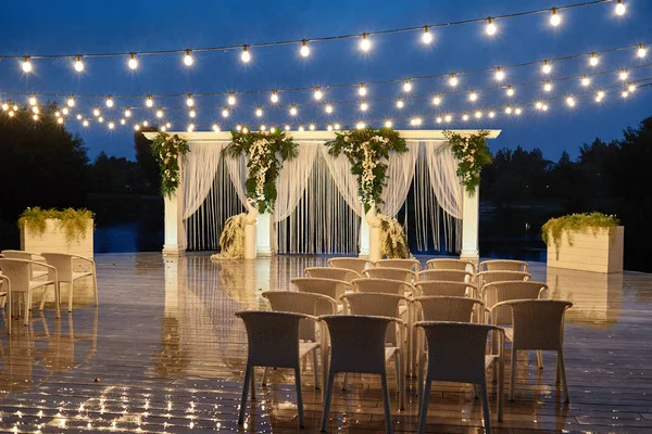 Night wedding ceremony with arch, orchid flowers, chairs and bul