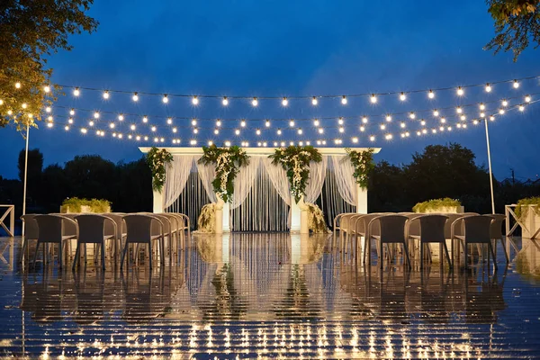 Night wedding ceremony with arch, orchid flowers, chairs and bul
