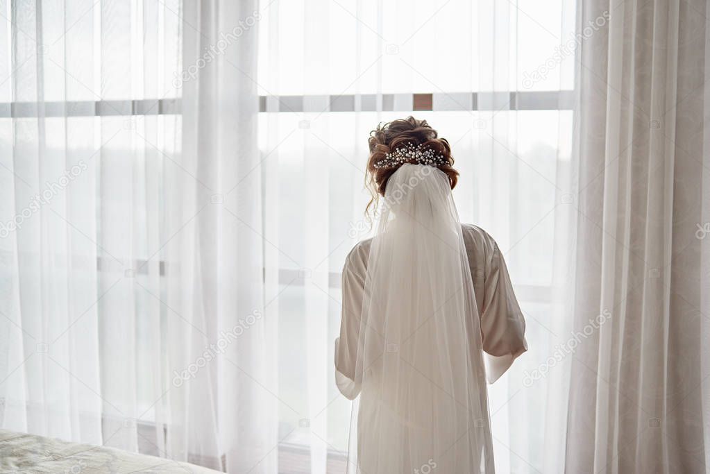 Portrait of beautiful bride in white silk dressing gown with cur