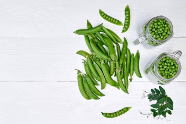 Kavanozda yeşil bezelye, bakla ve bezelye yaprakları beyaz ahşap masa backg