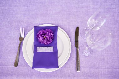 Beyaz tabaklar, çiçekler, şarap kadehleri ve çatal bıçak takımı ile masa ayarı