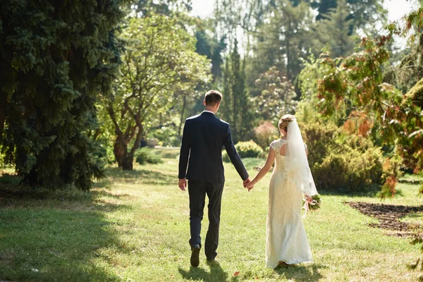 Feliz novia y novio tomados de la mano y caminando en el jardín en la boda —  Fotos de Stock