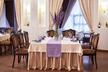 Beyaz tabaklar, şarap kadehleri, çatal bıçak takımı ve çiçekli masa ayarı