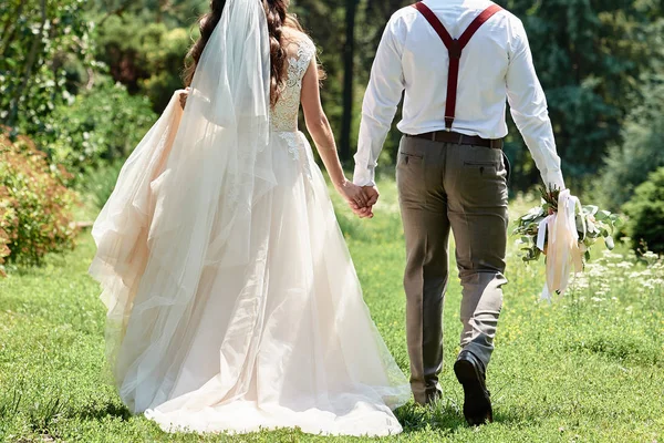 Feliz novia y novio tomados de la mano y caminando en el jardín en la boda —  Fotos de Stock