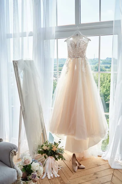 Schönes beiges Hochzeitskleid, das am Kleiderbügel am Fenster hängt — Stockfoto