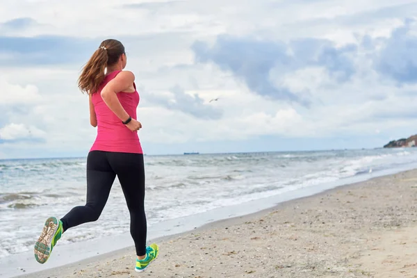 Back view of young fitness woman runner running at seaside, copy — Stock Photo, Image