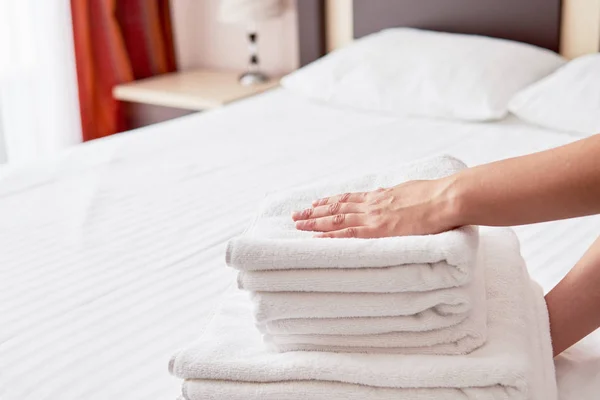 Mujer poniendo pila de toallas limpias de baño blanco fresco en la cama shee — Foto de Stock