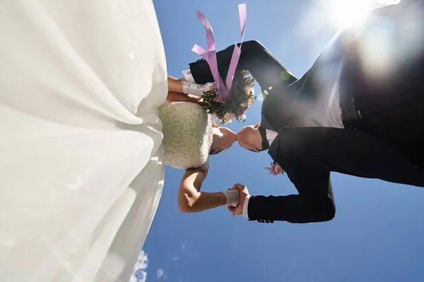 Glückliches Brautpaar hält Händchen und küsst sich vor blauem Himmel — Stockfoto