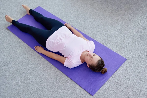 Young woman lying on yoga mat with eyes closed in savasana pose