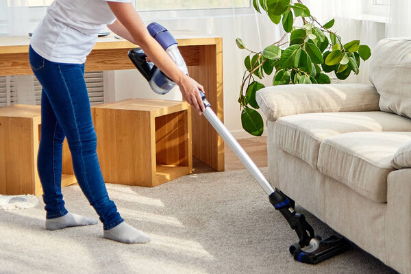 Portrait of young woman in white shirt and jeans cleaning carpet