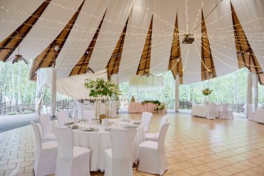 Masanın üzerinde çiçek demeti olan masa ayarları, kopyalama alanı. Lüks düğün resepsiyonunda. Restoranda verilen ziyafet için yuvarlak masa ve beyaz sandalyeler.