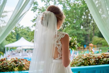 Beyaz gelinlik ve duvak giymiş güzel bir gelin. Terasta duruyor. Arka manzara, fotokopi odası. Gelin sabahı