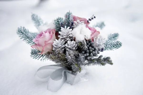 Winter wedding bouquet of pink roses, pine cones and christmas tree branches on snow, copy space