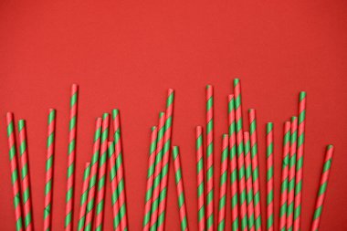 Kırmızı arka planda kırmızı ve yeşil çizgili pipetler, kopyalama alanı. Noel dokusu. Minimalizm kavramı. Üst manzara, düz uzanma